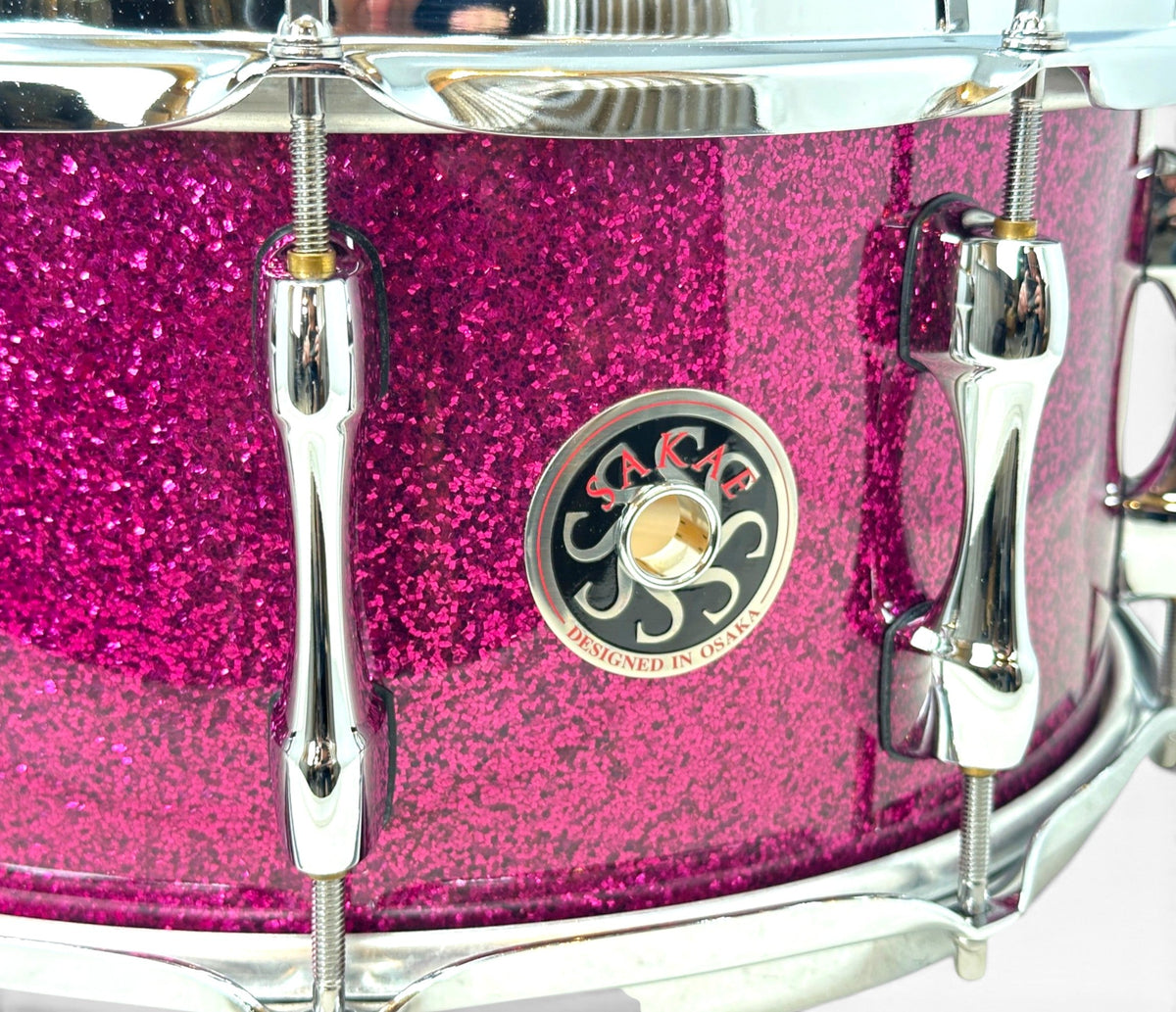 Sakae Evolved 14" x 6.5" Snare Drum in Magenta Sparkle – close-up of Sakae badge and sparkle finish